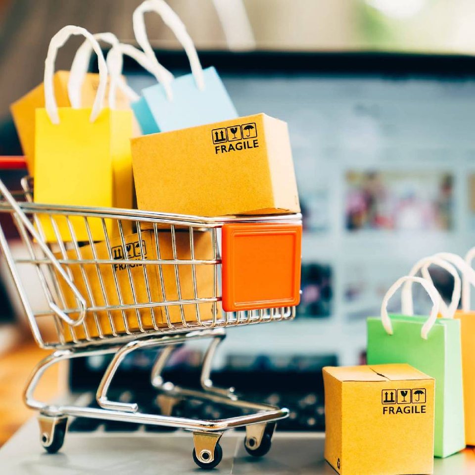 Shopping cart filled with colorful shopping bags in front of a laptop
